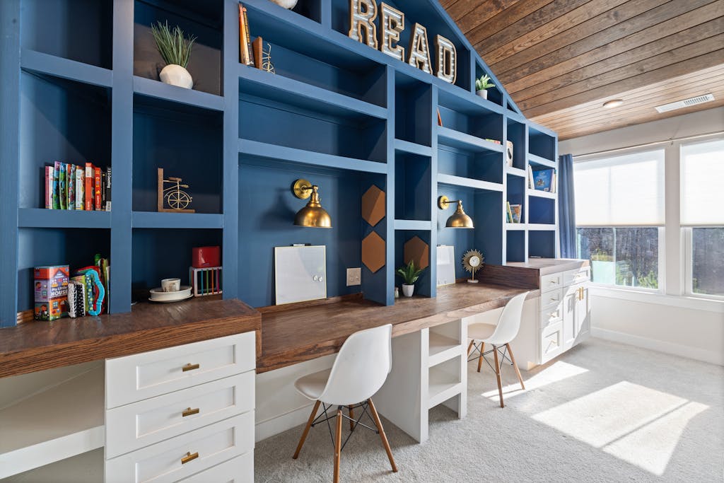 Bright home study room with custom blue bookshelves, wooden desk, and white chairs.